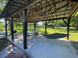 A covered outdoor area with a picnic table, chairs, a hammock, and a barbecue grill.