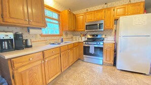 Una cocina con armarios de madera, estufa de acero inoxidable, microondas y refrigerador blanco.