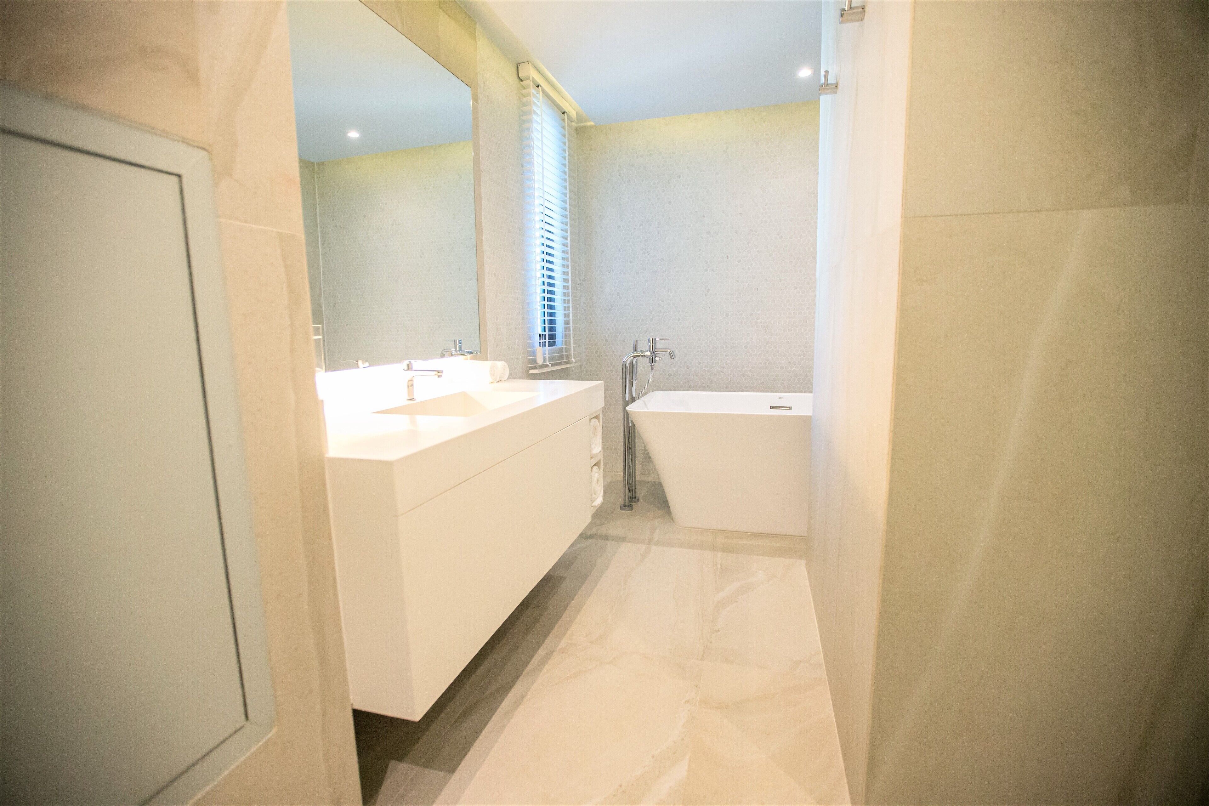 A modern bathroom with a large bathtub, two sinks, and a window with blinds.