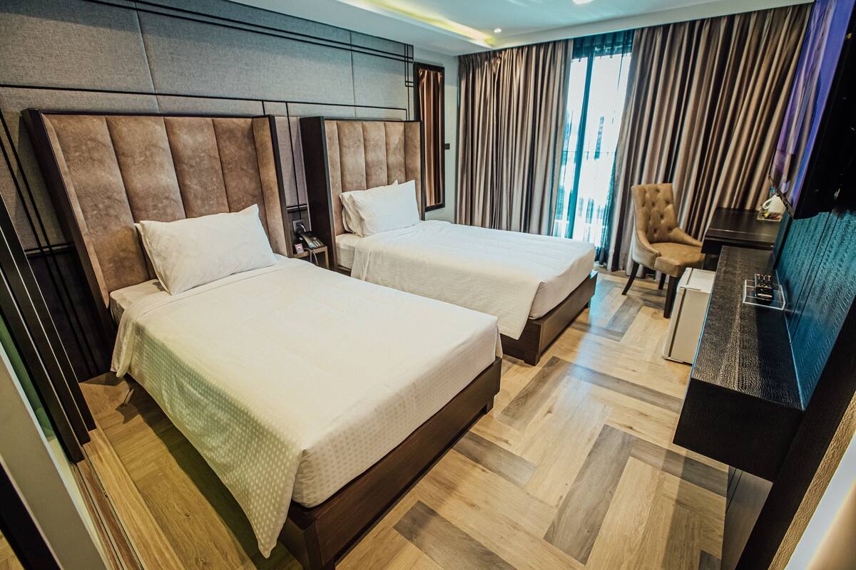 Ein Hotelzimmer mit zwei Betten, einem Schreibtisch, einem Sessel und einem Fernseher.