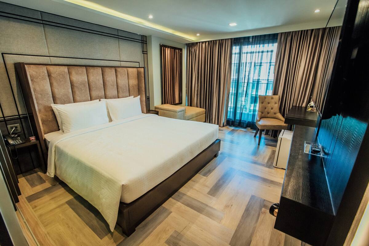 Ein Hotelzimmer mit einem großen Bett, einem Schreibtisch, einem Sessel und einem Fernseher.