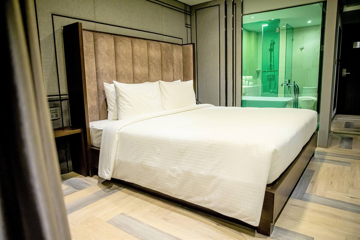 Ein modernes Hotelzimmer mit einem großen Bett, einem Holzkopfende, einer Duschkabine aus Glas und einem Holzboden.