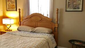 Une chambre à coucher avec un lit en bois, une lampe de chevet, une fenêtre avec des rideaux et deux tableaux encadrés accrochés au mur.