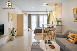 A modern hotel room with a bed, a dining area, a sofa, a TV, and a plant.