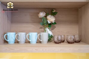 A wooden shelf with a vase of white flowers and six ceramic mugs in various colors.