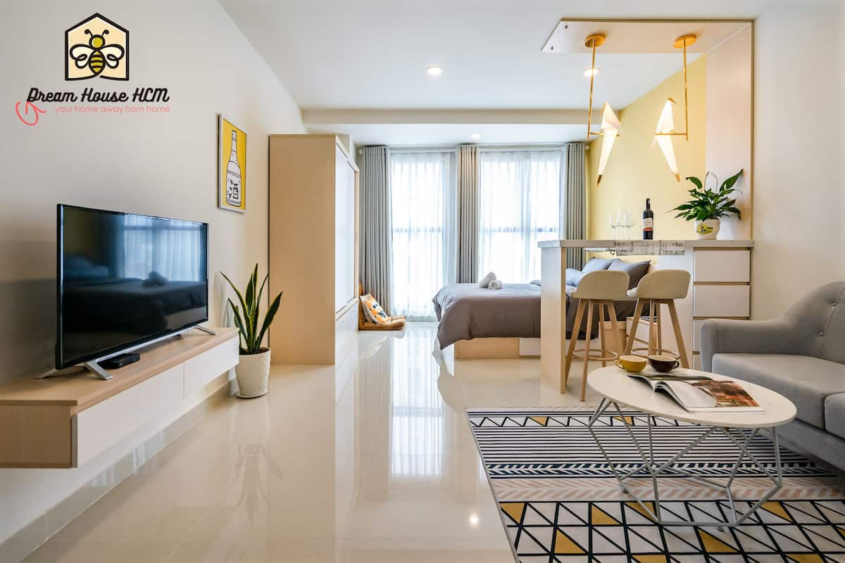 A modern hotel room with a flat-screen TV, a dining area, a sofa, and a large window with curtains.