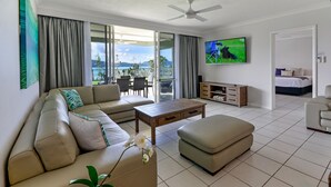 Uma sala de estar moderna com sofá, puf, mesa de centro e TV na parede.