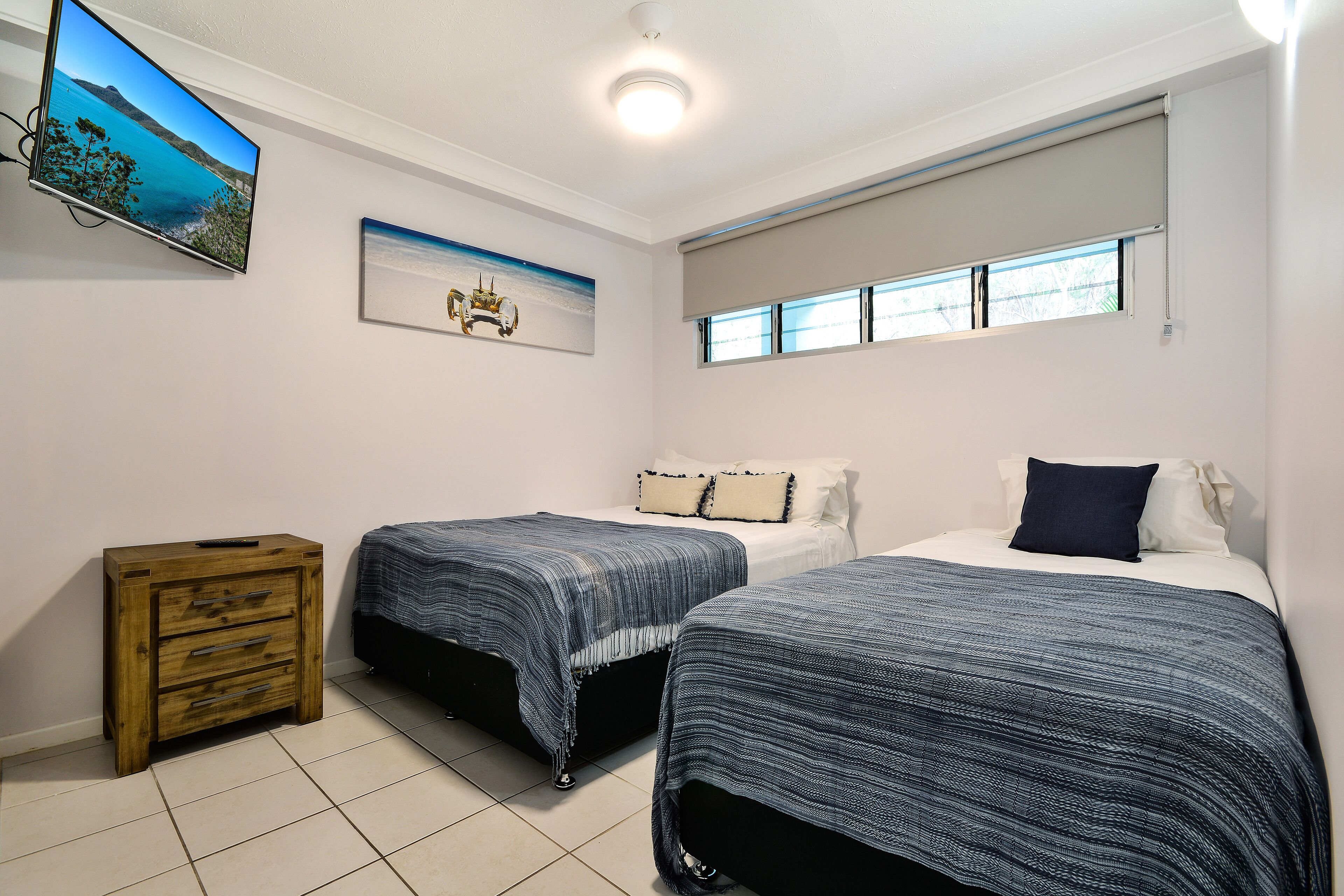 Un dormitorio con dos camas, un aparador de madera, un televisor y una ventana con persianas.