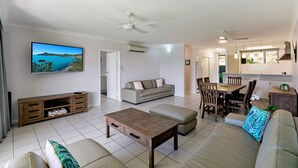 Uma sala de estar com sofá, mesa de centro, televisão e um espaço de jantar com cadeiras e mesa.