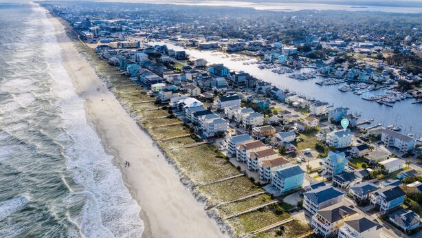 Vista aérea de uma área residencial costeira com casas à beira-mar e uma marina com barcos.