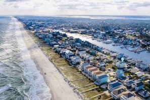 An aerial view of a coastal residential area with houses along the beach and a marina with boats.