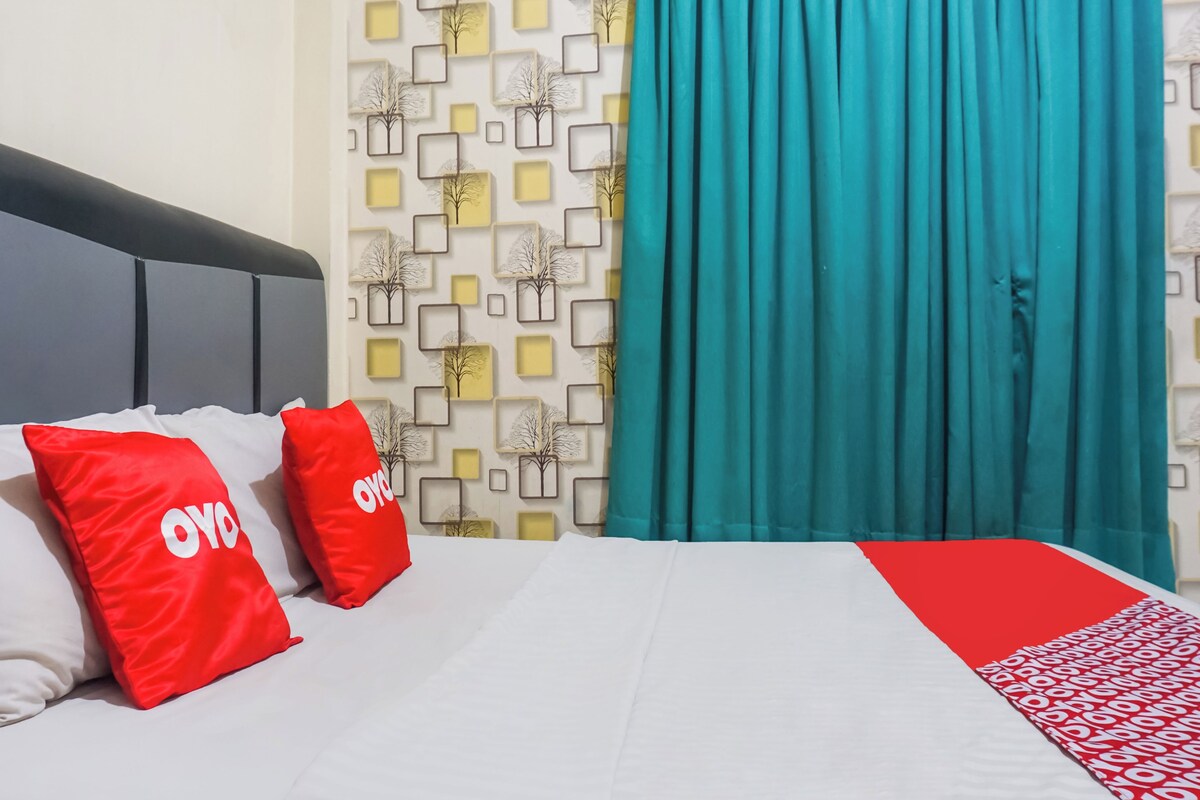 Habitación de hotel con una cama, dos almohadas rojas con el texto 'OYO', un papel tapiz estampado y cortinas color turquesa.
