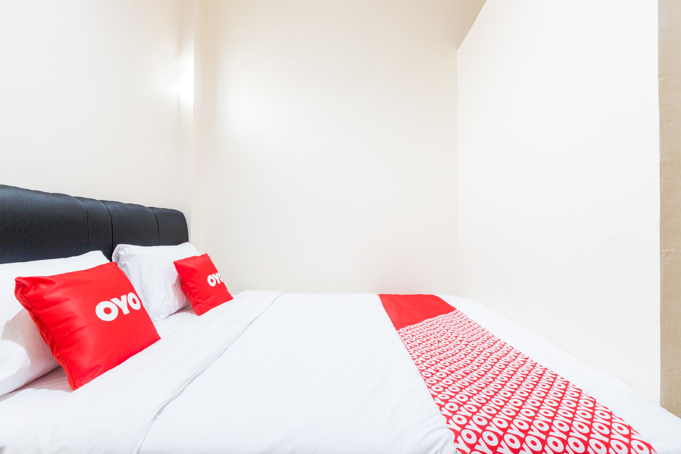 Cama com roupa de cama branca e detalhes vermelhos, incluindo almofadas e um cobertor.
