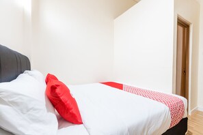 Una cama con ropa de cama blanca y roja, un cabecero gris y una puerta de madera al fondo.