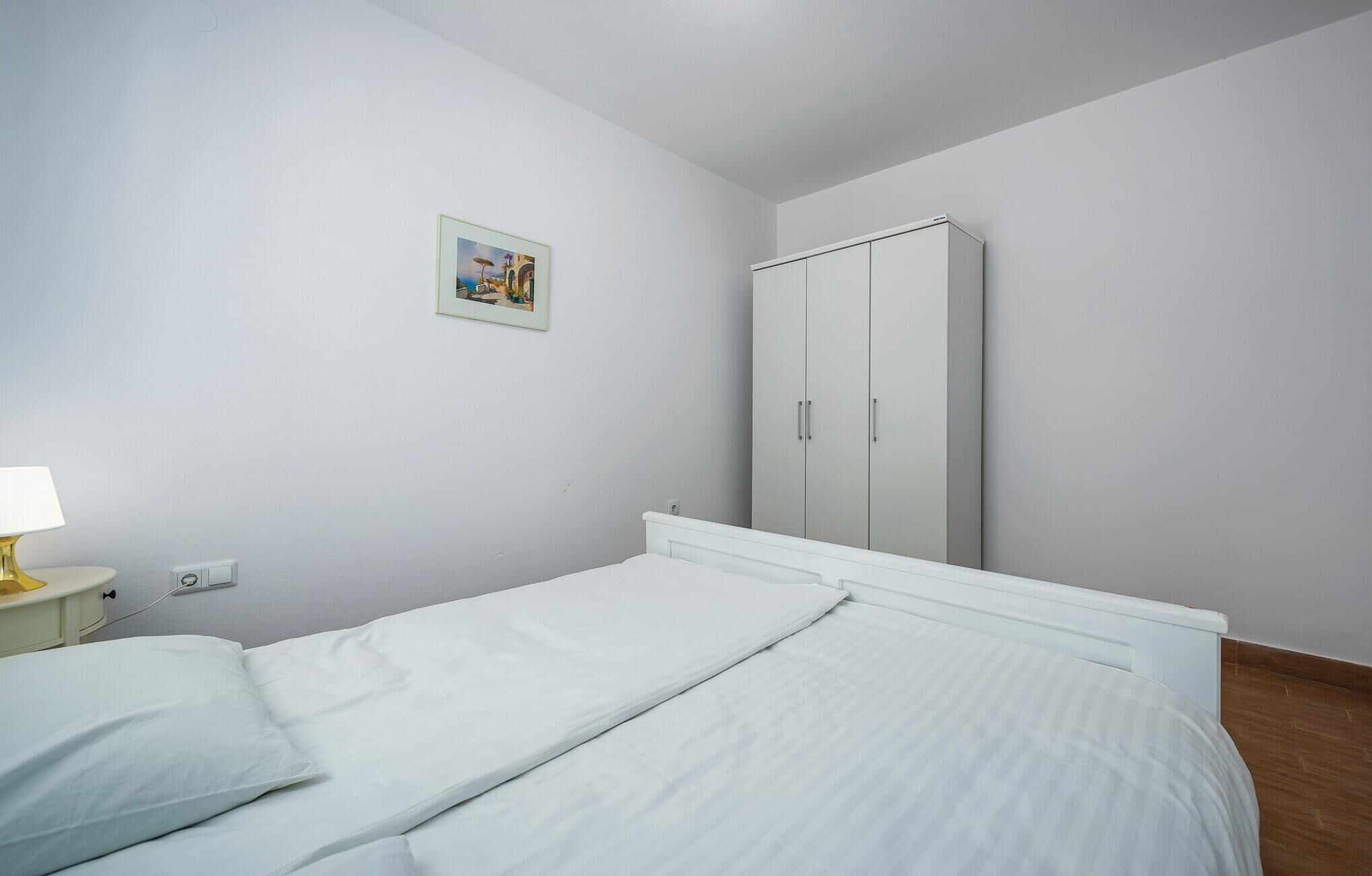 Un dormitorio con dos camas individuales, una mesita de noche con lámpara, un armario y un cuadro en la pared.