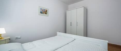 Un dormitorio con dos camas individuales, una mesita de noche con lámpara, un armario y un cuadro en la pared.
