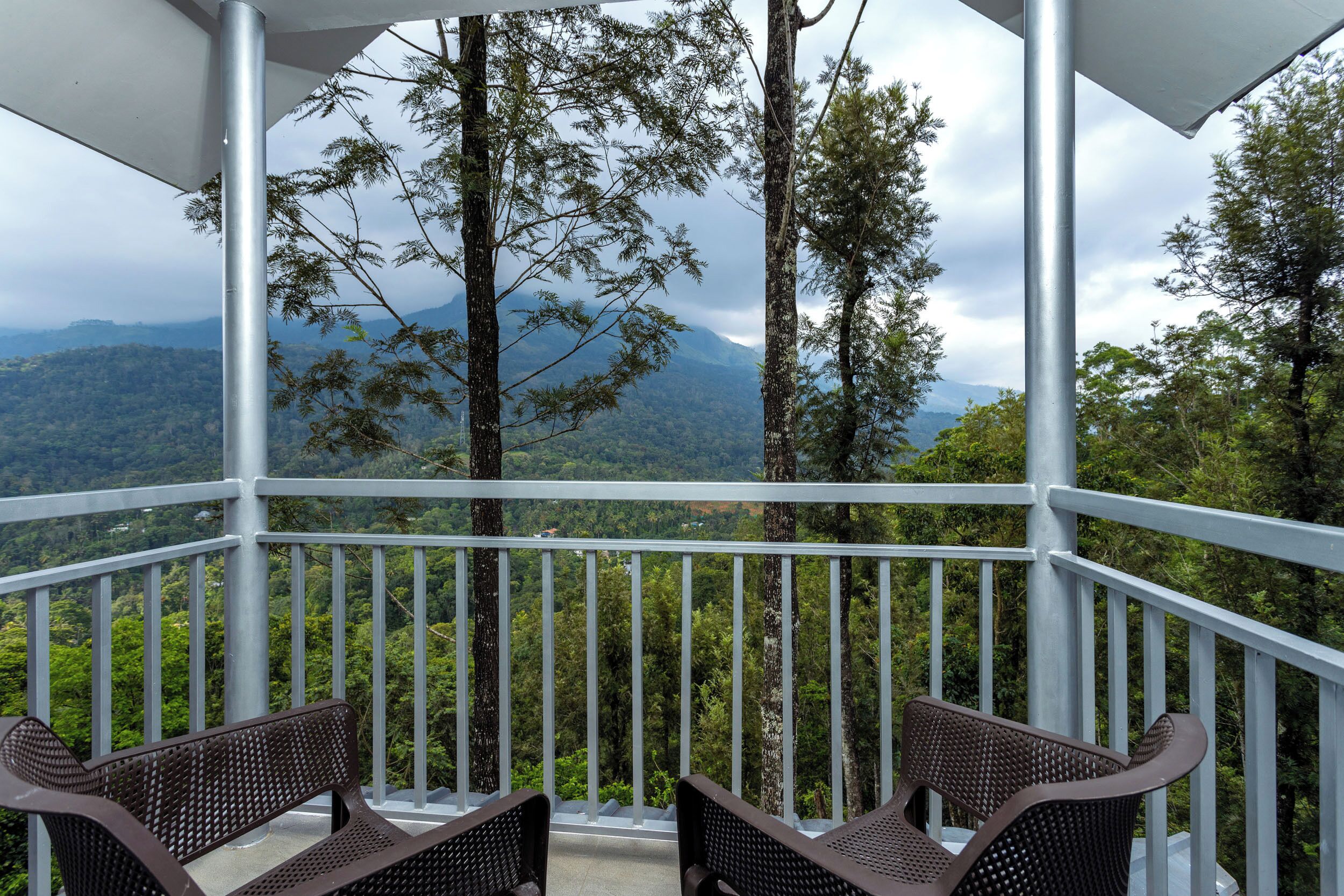 A covered outdoor area with two chairs and a railing, overlooking a mountainous landscape.