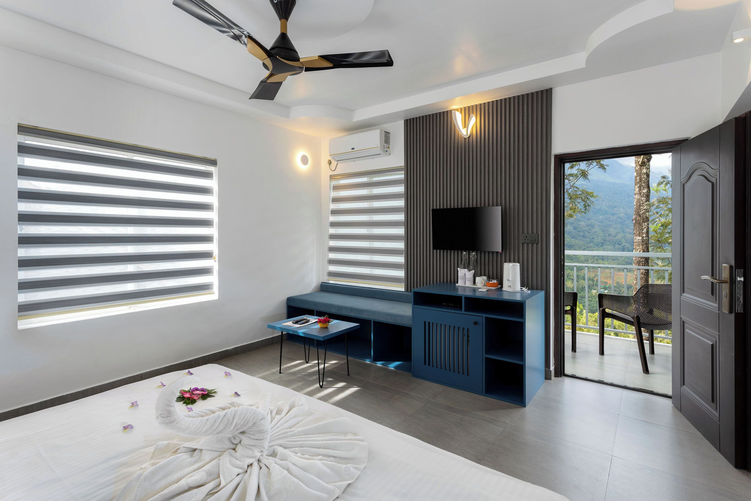 A modern bedroom with a bed, a desk, a TV, and a balcony with a view.