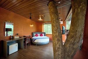 Un dormitorio con una cama, un escritorio y una silla. Se ve una ventana y el tronco de un árbol al frente.