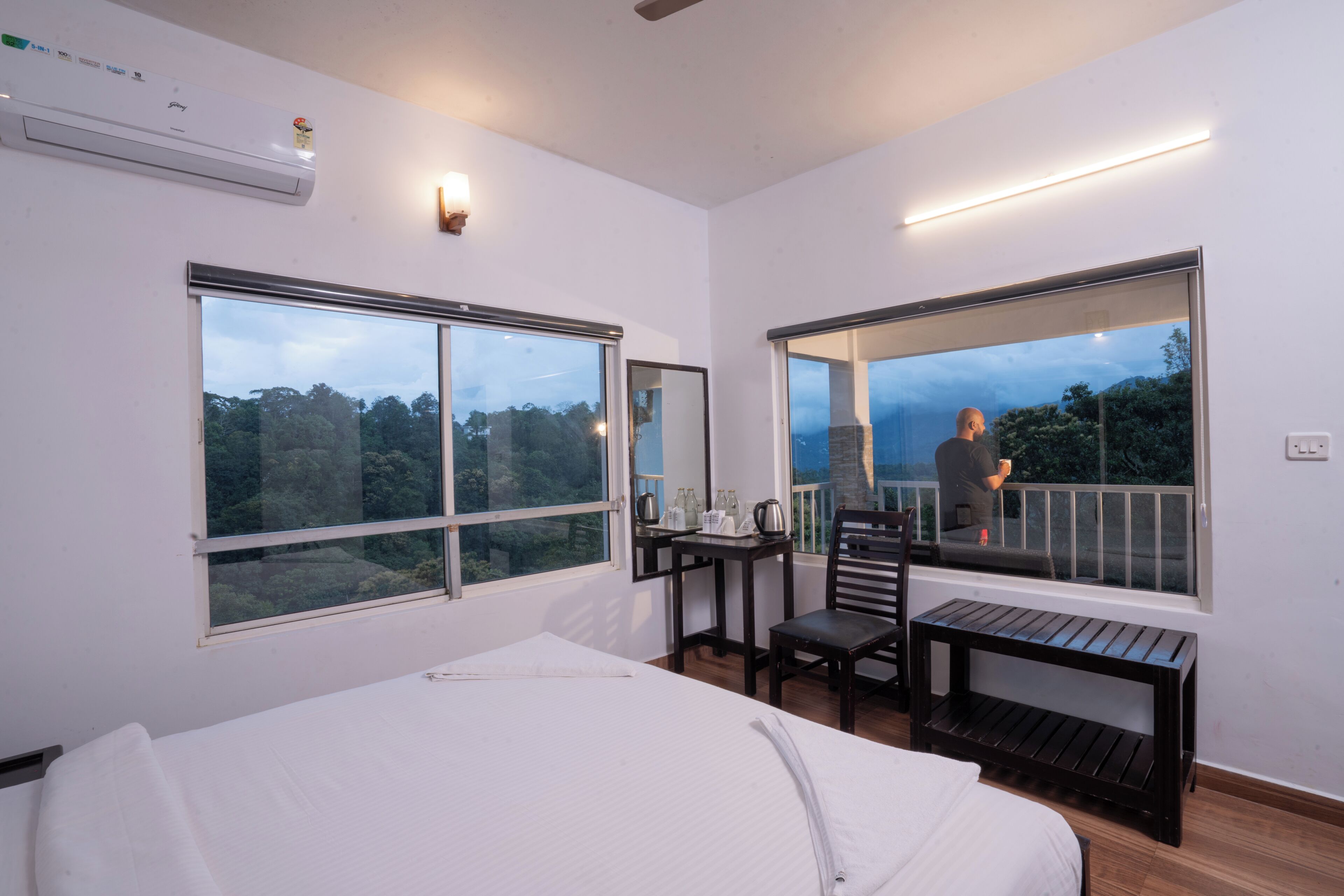 A hotel room with a bed, a desk, a chair, and a balcony with a view of the forest.
