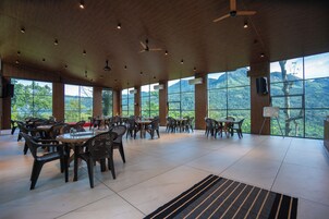 Amplio espacio interior con varias mesas y sillas, ventanas grandes que ofrecen vistas a un paisaje montañoso y ventiladores de techo.