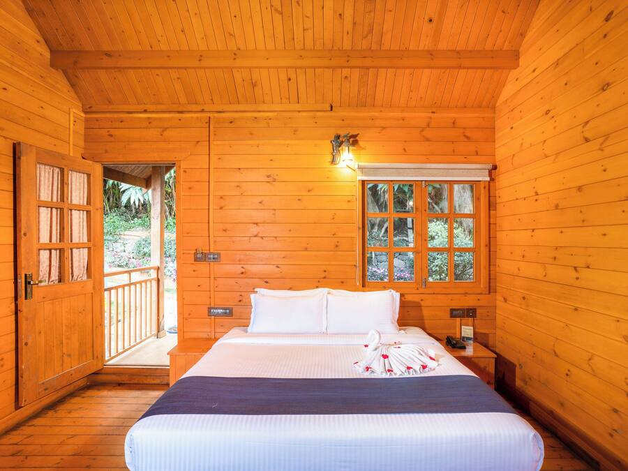 Quarto de madeira com cama, janela e porta que dá para o exterior.