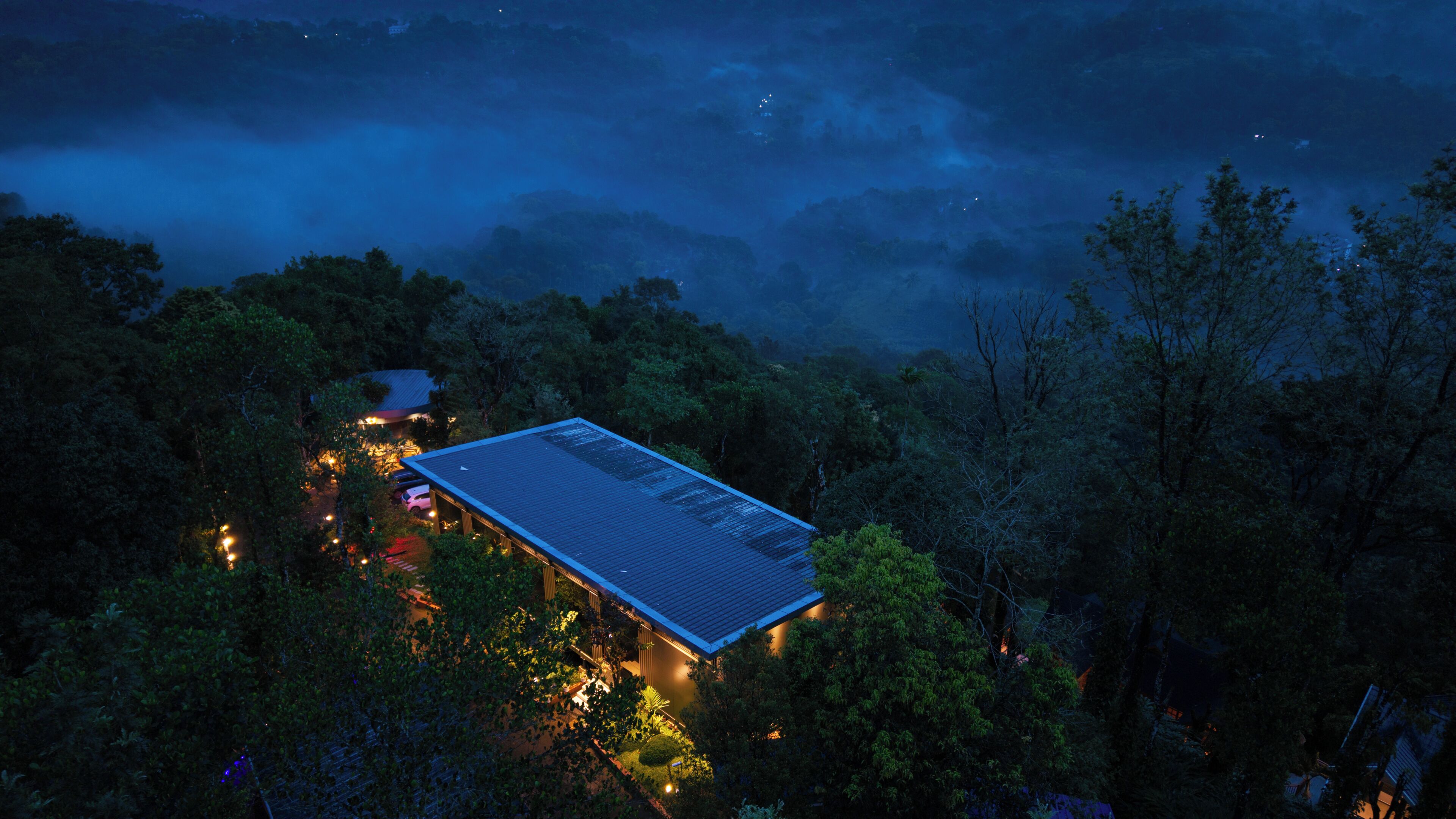 A building surrounded by dense forest with a flat roof and a small garden area.