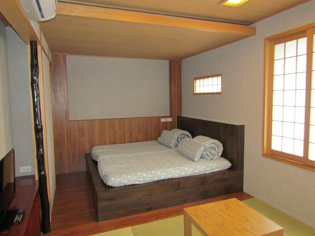 A small, compact room with a single bed, a wooden headboard, a small window, and a wooden table.