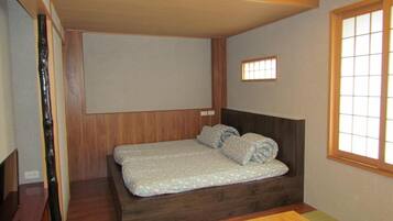 A small, compact room with a single bed, a wooden headboard, a small window, and a wooden table.