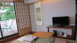Een traditionele Japanse kamer met tatami vloeren, een lage tafel, een televisie en een schuifdeur naar een buitenruimte.