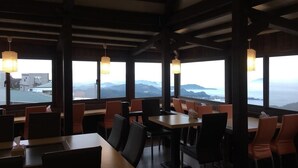 Een restaurant met hoge tafels en stoelen, grote ramen met uitzicht op de bergen, en hangende papieren lampions.