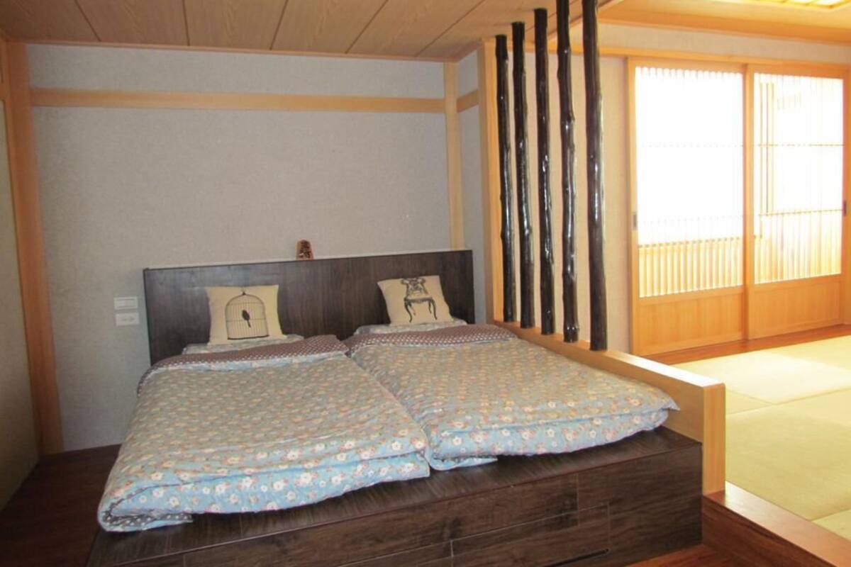 A double bed with floral bedding, a wooden headboard, and a sliding shoji screen.