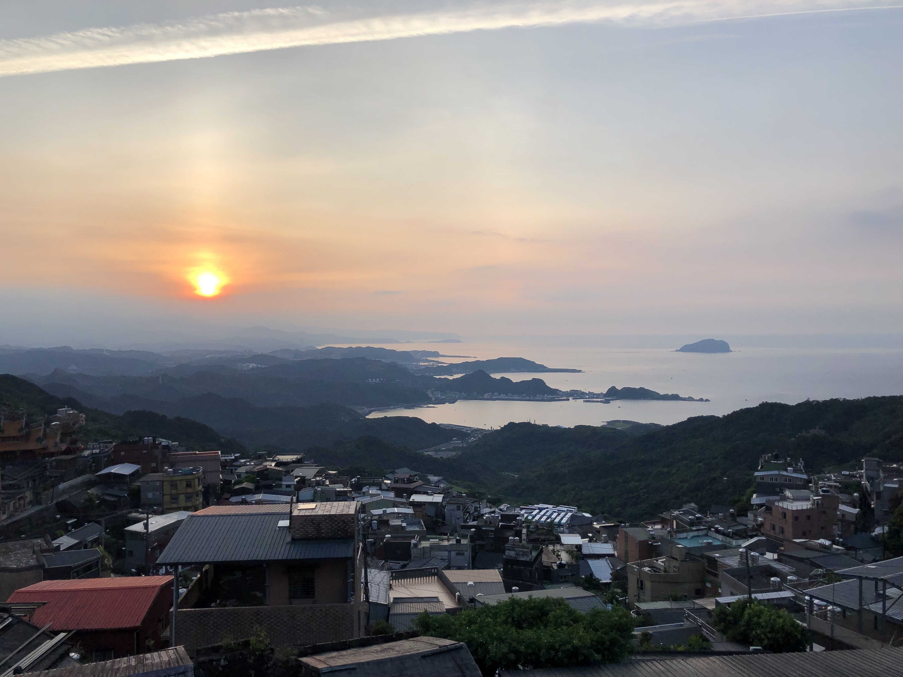 Une ville côtière au coucher du soleil, avec des bâtiments et une vue sur la mer.