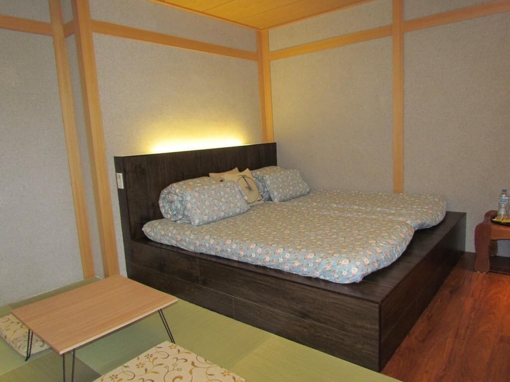 Un lit simple avec une tête de lit en bois, une table de chevet et une petite table placée devant le lit.