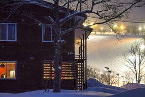 Ett trähus med en balkong, ett träd framför och ett snötäckt landskap.
