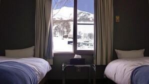 A hotel room with two beds, a window with curtains, a small table with a tissue box, and a view of a snowy landscape. - Annupuri Mountain View Lodge (Niseko)
