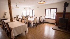 A dining area with tables and chairs, a fireplace, and large windows. - Annupuri Mountain View Lodge (Niseko)