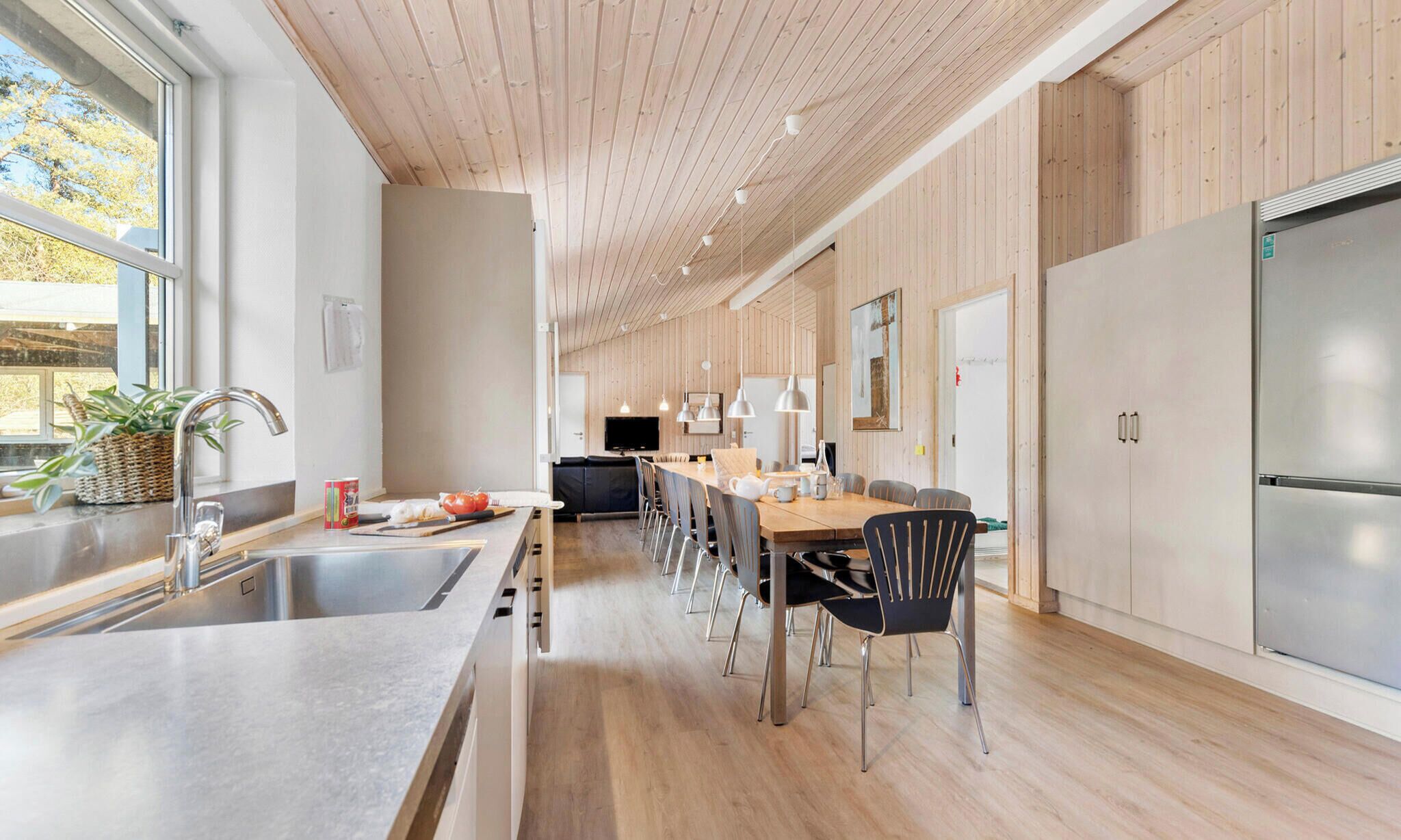 Een moderne keuken met houten wanden, een groot eiland met een spoelbak en een eetgedeelte met stoelen.