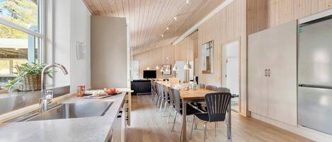 Een moderne keuken met houten wanden, een groot eiland met een spoelbak en een eetgedeelte met stoelen.
