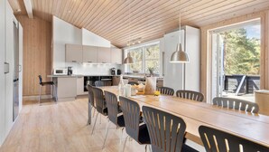 Eine moderne Küche mit Holzboden, weißen Schränken und einem Essbereich mit einem langen Tisch und Stühlen.