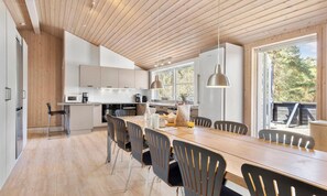 A modern kitchen with wooden ceiling, white cabinets, and a dining area with a long table and chairs.