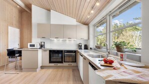 Eine moderne Küche mit Holzboden, weißen Schränken, einem eingebauten Ofen und einem großen Fenster mit Blick auf Bäume.