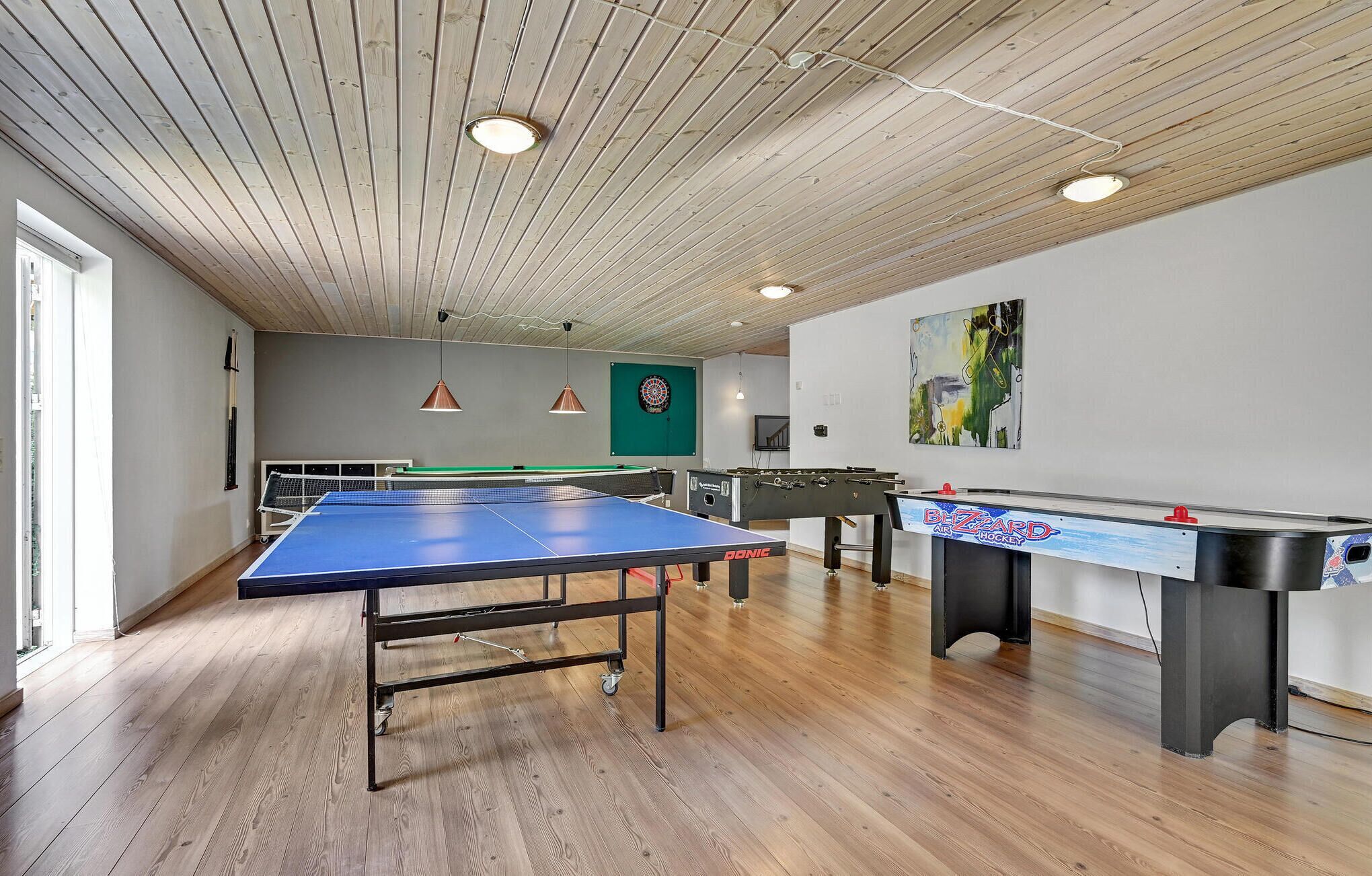 A room with a ping pong table, foosball table, dartboard, and a billiards table.