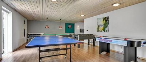 A room with a ping pong table, foosball table, dartboard, and a billiards table.