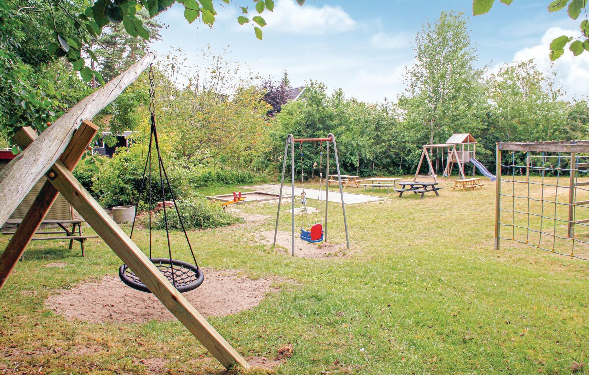 Une aire de jeux avec des balançoires, un toboggan, des tables de pique-nique et une structure en bois.