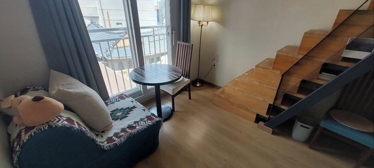 A cozy living area with a sofa, a round table, a lamp, and a staircase.