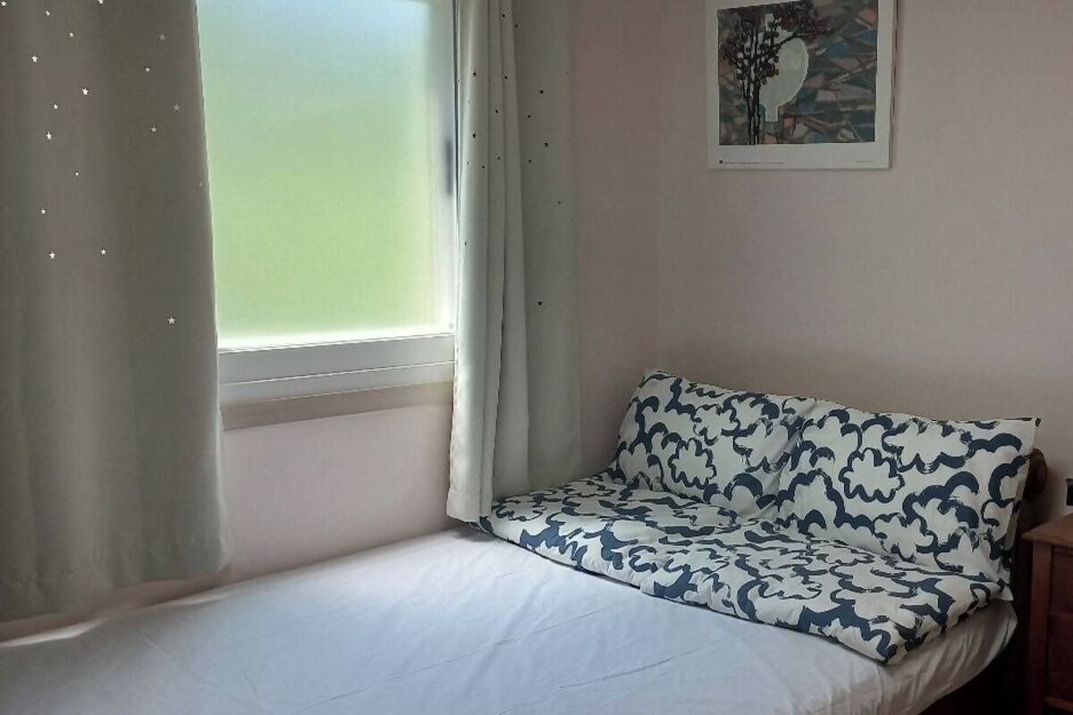 A small bedroom with a single bed, a dresser, a mirror, and a window with curtains.
