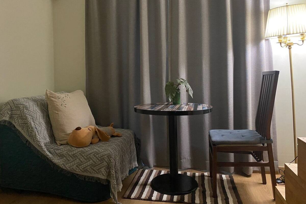 A cozy living area with a sofa, a small round table with a plant, a lamp, and a chair.