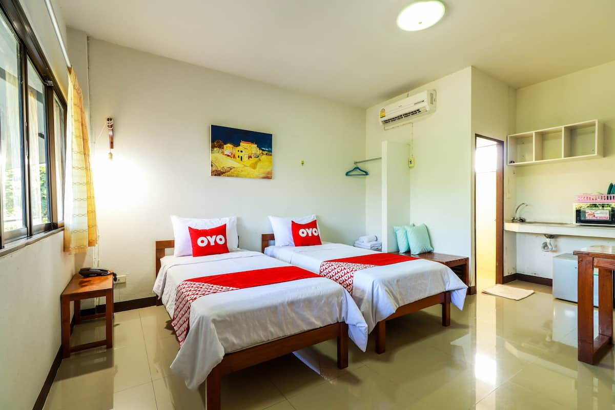 Une chambre d’hôtel avec deux lits, une petite table, un bureau, un lavabo et une fenêtre avec des rideaux.
