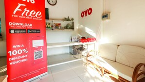 Une pièce avec un canapé blanc, un bureau avec un ordinateur et un panneau publicitaire rouge.